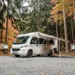 Camping-car blanc garé sur l'aire gratuite proche de la cascade du Hérisson dans le Jura, entouré de forêt automnale