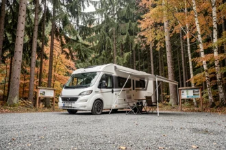 Camping-car blanc garé sur l'aire gratuite proche de la cascade du Hérisson dans le Jura, entouré de forêt automnale