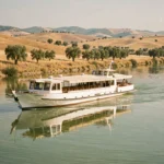 Bateau de croisière fluviale naviguant sur une rivière espagnole entourée de collines dorées et d'oliviers