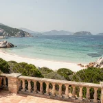 Terrasse d'hôtel en Corse avec vue panoramique sur une plage aux eaux turquoise et sable blanc
