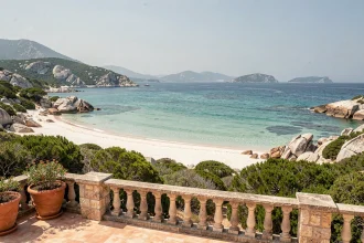 Terrasse d'hôtel en Corse avec vue panoramique sur une plage aux eaux turquoise et sable blanc