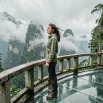 Voyageuse sur le skywalk de verre de la montagne Tianmen à Zhangjiajie, entourée de pics karstiques et de brume, lors d'un road trip au Hunan en Chine